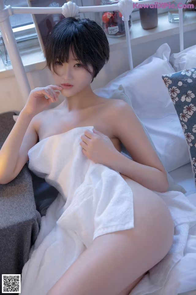 A naked woman sitting on a bed covered in a towel.