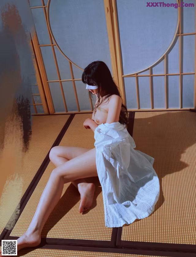 A woman sitting on a tatami mat in front of a window.