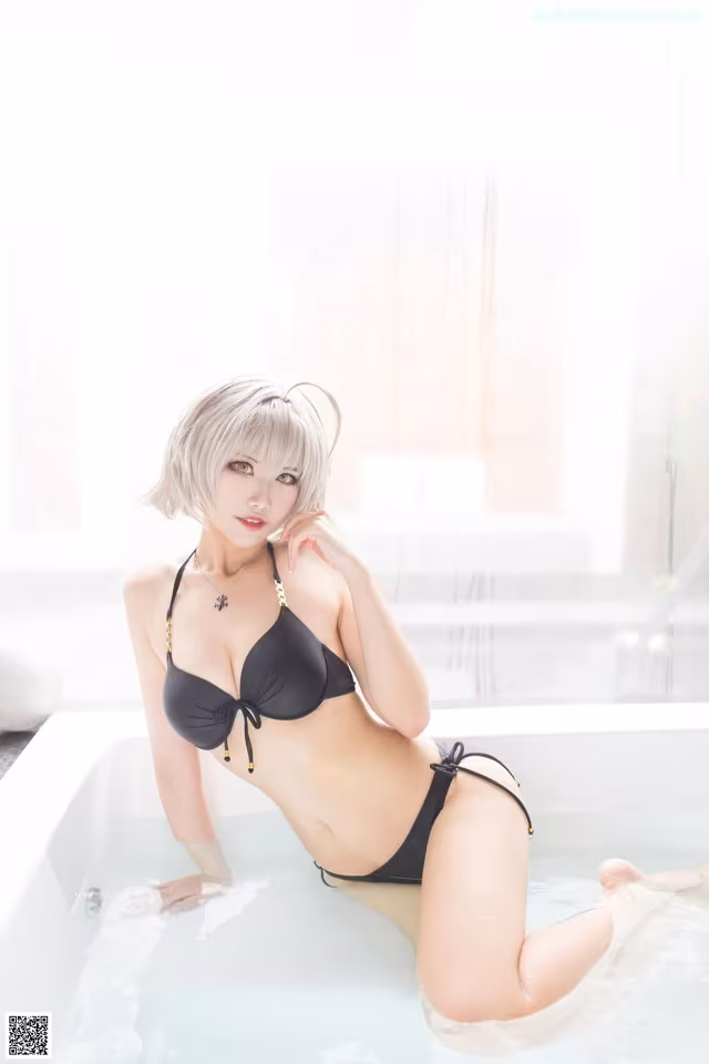 A woman in a black bikini sitting in a bathtub.