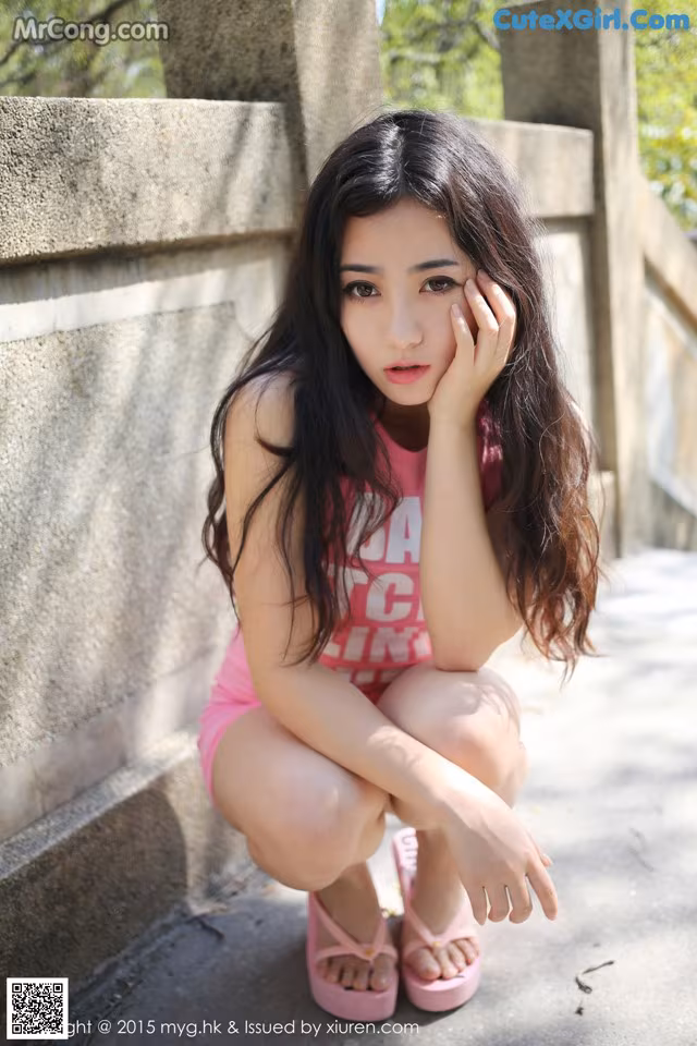 A young woman in a pink bathing suit crouching down on the ground.