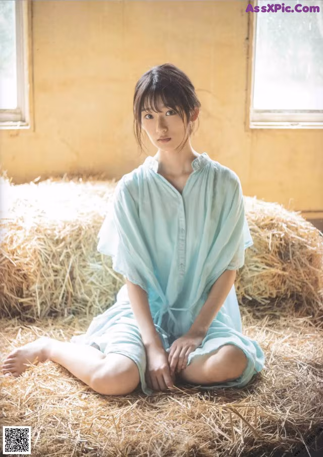 A woman sitting on a pile of hay in a room.