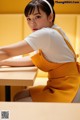 A woman sitting at a table in a yellow apron.