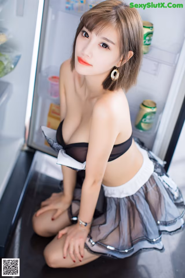 A woman in a black and white dress sitting in front of a refrigerator.