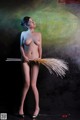 A naked woman holding a broom in front of a painting.