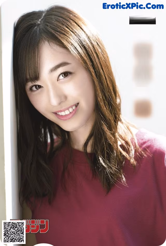 A woman in a maroon shirt leaning against a wall.