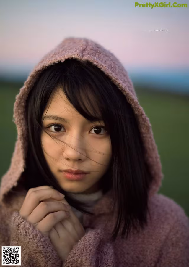 A young woman in a pink hooded jacket is posing for a picture.