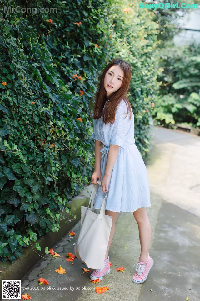 A woman in a blue and white striped dress holding a white bag.