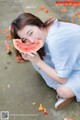 A woman sitting on the ground eating a slice of watermelon.