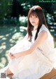 A woman in a white dress sitting on a wooden bench.