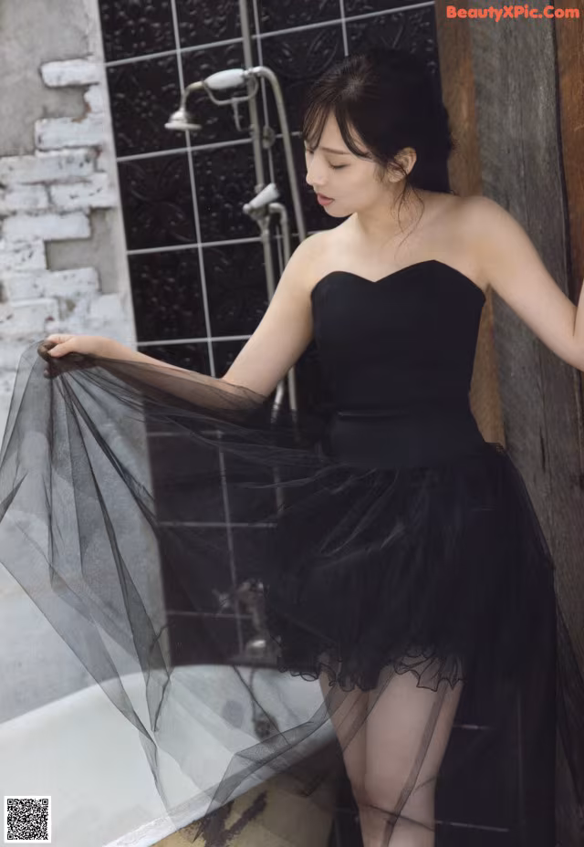 A woman in a black dress standing in a bathtub.