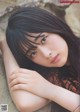 A woman with long black hair leaning against a rock.